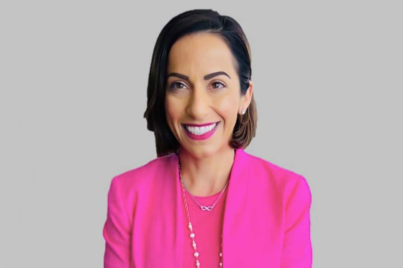 A woman in a vibrant pink blazer with a necklace and a grey background.